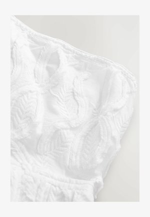 Bílá látka s texturovanými, vyšívanými vzory listů. Měkký, lehký materiál s detailními výšivkami podél okrajů.