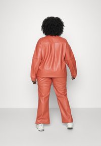Coral leather outfit featuring an oversized jacket and matching pants. Soft texture, long sleeves, and flared pant legs. White sneakers.