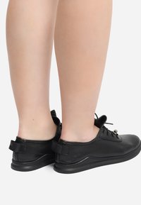 Schwarze, strukturierte, durchstochene Schuhe mit niedrigem Profil, versehen mit einer Schnürung und kleinen Fersenschlaufen. Glatte Gummisohlen.