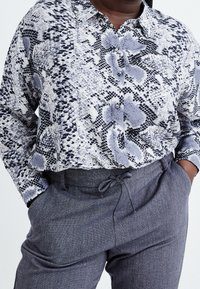 Knapp-up skjorta i ett ormtrycksmönster, grå och svart med en texturerad yta. Kombination med grå byxor med dragsko i midjan.