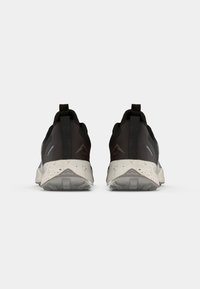 Zwarte sportieve schoenen met een textuur, reflecterende accenten en een grijze gevlekte zool. Voorzien van een trekband aan de achterkant voor gemakkelijk aan- en uittrekken.