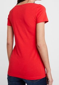 Camiseta roja de manga corta hecha de algodón suave. Presenta un escote redondo y un dobladillo ligeramente curvado en la parte posterior.