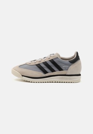 Baskets Adidas SL 72 à profil bas avec daim beige clair, tissu gris et trois bandes noires sur une semelle blanche rainurée.