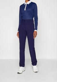 Námořnicky modré polo s dlouhým rukávem a bílým límečkem, doplněné námořnicky modrými kalhotami a bílými sportovními botami. Oblečení má přiléhavý střih a hladkou strukturu.