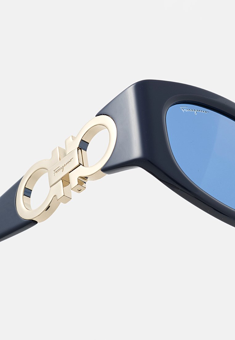 Sonnenbrille mit blauen, getönten Gläsern, dunkelblauen Kunststoffrahmen und einem goldfarbenen Hardware-Element an den Schläfen mit einem verwobenen Design.