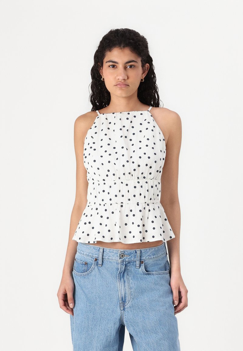 Weißes Top mit Trägern und schwarzen Punkten, gerafftem Bund und weit schwingendem Peplum-Saum. Aus leichtem Material gefertigt. Verstellbare Träger.