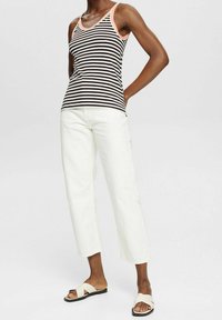 Randig linne i svart och vitt med en persikofärgad halsringning, tillsammans med vita capribyxor och neutrala sandaler.