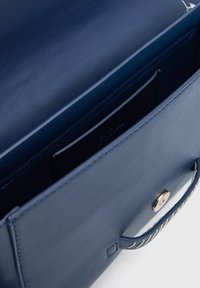 Navy leren handtas met een gladde structuur, zilveren accenten en een enkele handgreep met decoratieve stiksels. Interieurvakjes zijn zichtbaar.