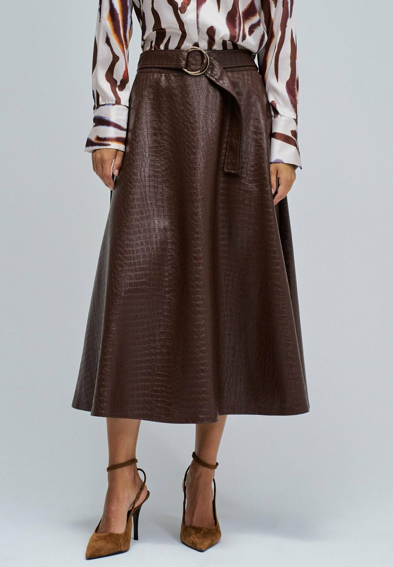 Falda midi marrón con estampado de cocodrilo, con cintura ceñida y abertura frontal. Combinada con zapatos de tacón alto de ante color cuero.