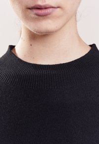 Czarny sweter dzianinowy z okrągłym dekoltem, z prążkowaną teksturą wokół kołnierza. Zbliżenie na szyję i brodę.