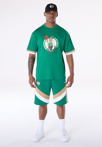 Πράσινο κοντομάνικο πουκάμισο και αντίστοιχα σορτς με το λογότυπο των Boston Celtics. Διαθέτουν λευκές και μπεζ λεπτομέρειες, κατασκευασμένα από αναπνεύσιμο ύφασμα. Λευκά αθλητικά παπούτσια.