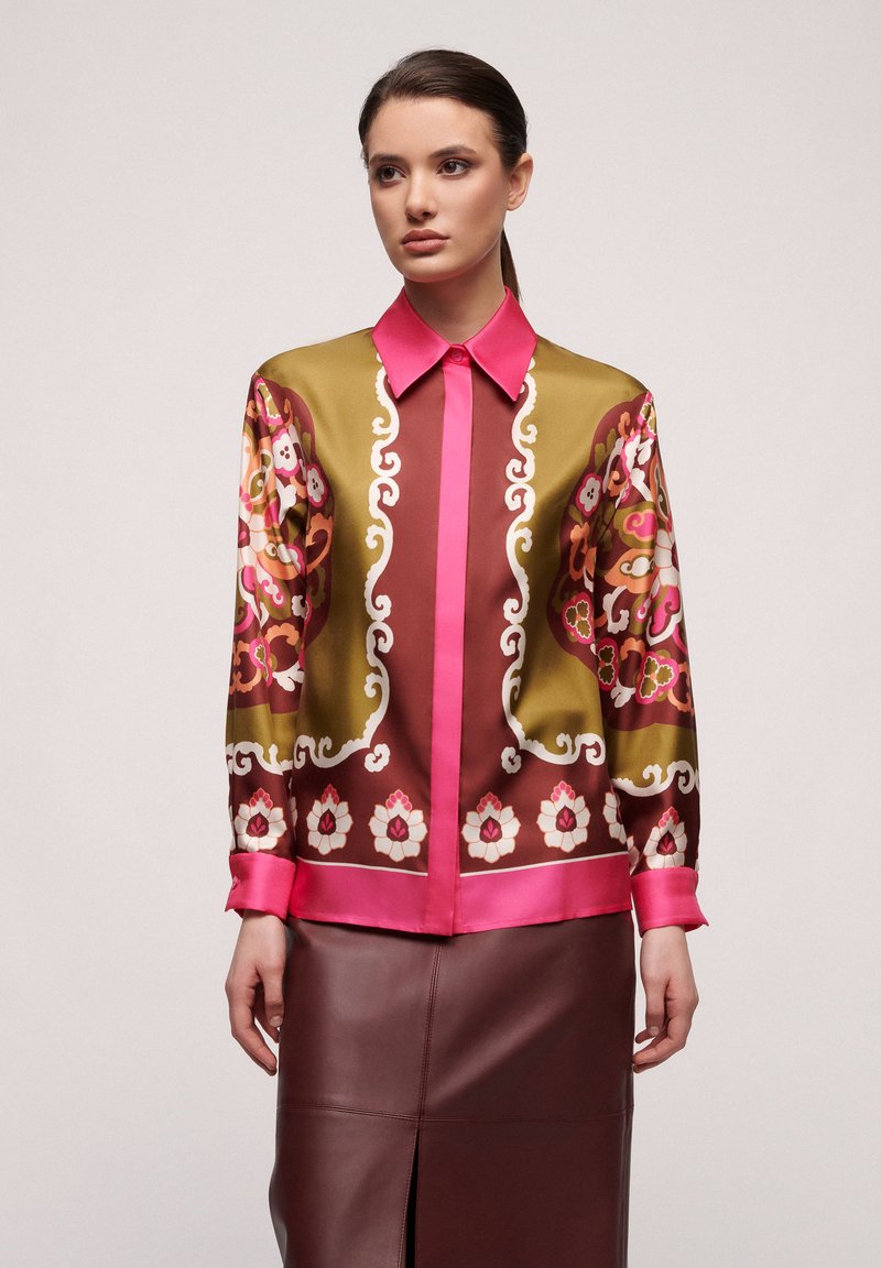 Blouse transparente avec un motif floral en rose, marron et vert, dotée d'un col et de poignets roses. Assortie à une jupe en cuir marron.