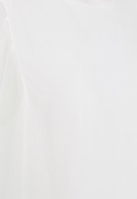 Haut blanc à manches courtes avec une texture lisse et un col rond. Présente des détails froncés subtils au niveau des épaules.