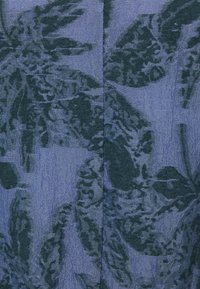 Tissu bleu avec motif jacquard floral bleu marine foncé et détail de couture centrale visible.