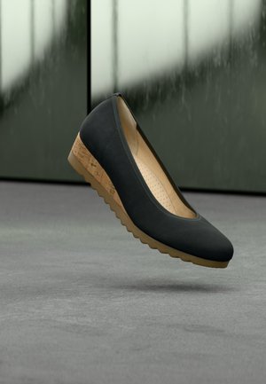 Čierna plochá topánka s zaokrúhlenou špičkou, štruktúrovaným zvrškom a strednou časťou podrážky zdobenou korkom. Má gumovú podrážku s vlnitým vzorom.