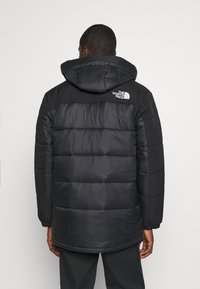 Melnā pūkaina jaka ar kapuci, krokota tekstūra, elastīgi aproces un "The North Face" baltais logos augšējā aizmugurē.
