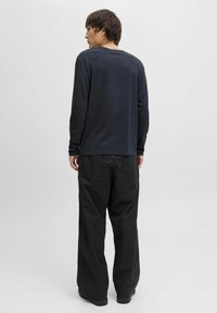 Zwarte longsleeve shirt met een royale pasvorm en ronde halslijn, gecombineerd met zwarte wide-leg broeken, beide met een gladde stof en zonder patronen.