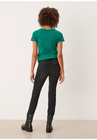 Camiseta verde de manga corta y jeans ajustados negros, combinados con botas negras hasta la rodilla. Diseño simple con un ajuste casual y un mínimo de detalles.