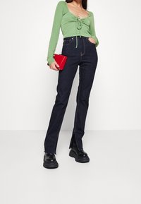 Maglietta verde a maniche lunghe con dettaglio a fiocco sul davanti, abbinata a jeans a vita alta blu scuro con fessure laterali e stivali con piattaforma neri.