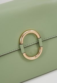 Borsa a tracolla rettangolare in pelle verde con superficie liscia, dotata di una chiusura ovale dorata e cuciture coordinate lungo i bordi.