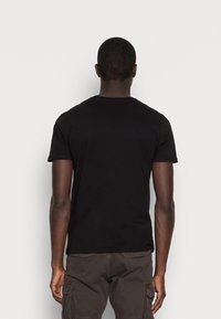 Osoba odwrócona plecami, ubrana w prostą czarną koszulkę z krótkim rękawem oraz ciemne spodenki cargo, na białym tle.