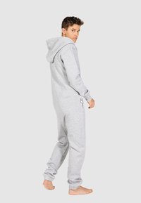 Grijze katoenen hoodie-jumpsuit met lange mouwen, trekkoord en elastische boorden, van opzij weergegeven tegen een neutrale achtergrond.