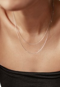 Collier en argent à plusieurs couches présentant deux fines chaînes, l'une légèrement plus longue que l'autre, reposant sur une clavicule nue, contre un haut sombre.