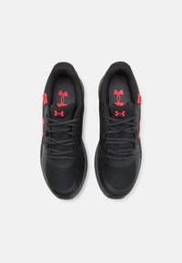 Pantofi sport negri cu o parte superioară texturată, având accente și logo-uri roșii, design cu șireturi și o talpă bine îmblănită.