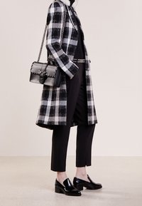 Černobílý kostičkovaný dlouhý kabát přes černé kalhoty a svetr, doplněný černou kabelkou na řetízku a černými koženými mokasíny.