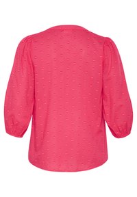 Blouse rose avec des manches bouffantes, arborant un motif texturé de petits cœurs sur tout le vêtement. Encolure ronde et ourlet légèrement arrondi.