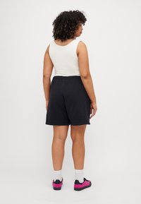 Baltas be rankovių marškinėliai, juodos šortai su elastingu juosmeniu. Modelis vilki rožinius ir juodus batus su baltais kojiniais, garbanoti plaukai natūraliai suformuoti.