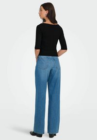 Sort ribbet long-sleeve top kombineret med højtaljede lys blå wide-leg jeans. Jeansene har to baglommer og et lige snit.