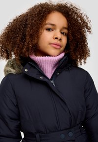 Navy-Puffermantel mit einem mit Fell gefütterten Kapuze, getragen über einem pinkfarbenen gerippten Rollkragenpullover. Verfügt über eine taillierte Form und einen Druckknopfverschluss.