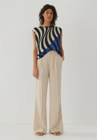 Locker sitzendes Oberteil mit marineblauen und cremefarbenen Streifen, kurze Ärmel, kombiniert mit beigen, weit geschnittenen Hosen. Weiche Texturen und entspannte Silhouette.