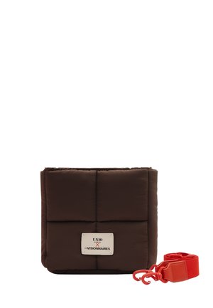 Quadratische, gepolsterte dunkelbraune Tasche mit weißem Etikett und separatem, abnehmbarem, leuchtend rotem Tragegurt mit Haken auf weißem Hintergrund.