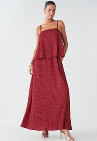 Makowa, bezrękawnikowa sukienka maxi z teksturowanym wzorem kratki, warstwowym krojem i zwiewną sylwetką. Połączona z metalicznymi butami.