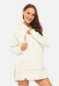Cream-colored fluffy oversized hoodie with a kangaroo pocket, side slits, and fabric texture resembling soft fleece. Hooded design.