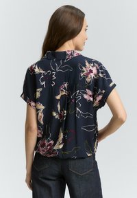 Blusa floreale blu navy con maniche corte, caratterizzata da un motivo di fiori multicolore e una vestibilità comoda. Dettaglio della spallina sul retro e texture del tessuto morbida.