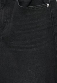 Μαύρο τζιν ύφασμα με μαλακή υφή, που διαθέτει πλαϊνή τσέπη και λεπτομέρεια ασημένιου μεταλλικού κουμπώματος κοντά στη μέση.