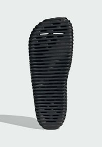 Svart sko med ribbat mönster, med horisontella spår och en böjd form. Materialet verkar flexibelt och texturerat.