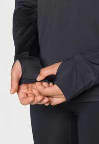 Μακρυμάνικη αθλητική μπλούζα από μαύρο ύφασμα. Διαθέτει θηλάκια για τους αντίχειρες στους καρπούς, εφαρμοστή σχεδίαση και απαλό ύφασμα. Ιδανική για αθλητική ένδυση.