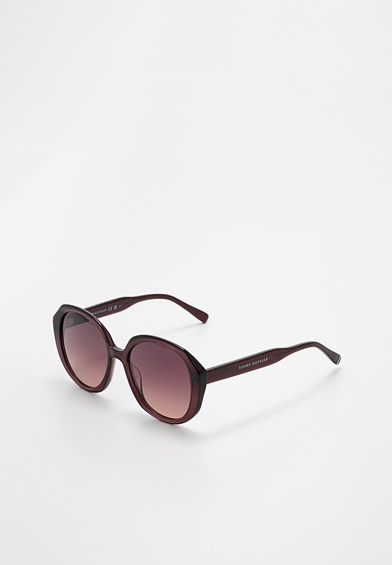 Dark purple oversized round sunglasses with gradient lenses and "Tommy Hilfiger" branding on the temples, on a white background.