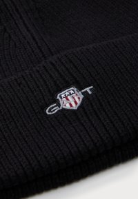 Bonnet en tricot noir avec une texture côtelée et un patch logo brodé coloré avec des étoiles et des rayures.