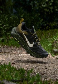 Αθλητικά παπούτσια Nike για τρέξιμο με άνω μέρος από υφασμάτινο ύφασμα σε μαύρο και ελιά, λευκό λογότυπο, σόλα με μαύρες και πράσινες βούλες, υφασμάτινα κορδόνια με υφή και λάστιχο για τράβηγμα.