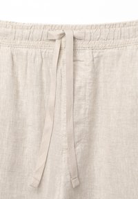 Beige kangaspantsit, joissa on joustava vyötärö ja nyöri, kevyttä materiaalia ja yksinkertainen muotoilu.