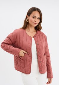 Giacca trapuntata di colore rosa tenue con scollatura rotonda, bottoni a pressione e tasche laterali; presenta cuciture verticali per texture.