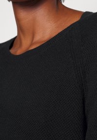 Maglione nero in tessuto strutturato con collo a coste e una vista ravvicinata del motivo a maglia del tessuto.