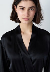 Robe in raso nero con colletto a scialle, caratterizzata da una texture liscia e senza fantasie visibili. Il capo ha una vestibilità rilassata.