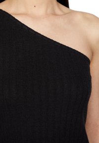 Top negro de canalé asimétrico, tejido de punto, que presenta un diseño de un solo hombro y una textura sutil. Sin herrajes ni acentos visibles.