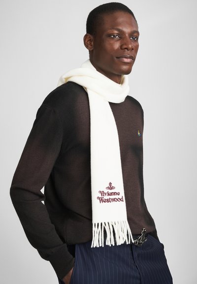 Bela volnena ruta s resečnimi konci, ki ima bordo vezenje "Vivienne Westwood". Nosi se čez temno teksturirano pulover.